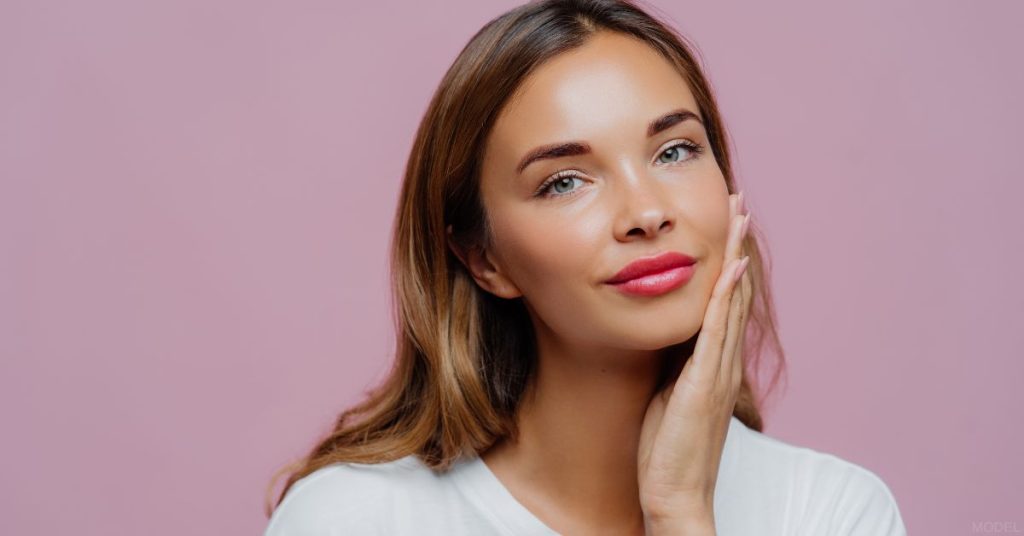 Woman smiling and gently touching her face (MODEL)