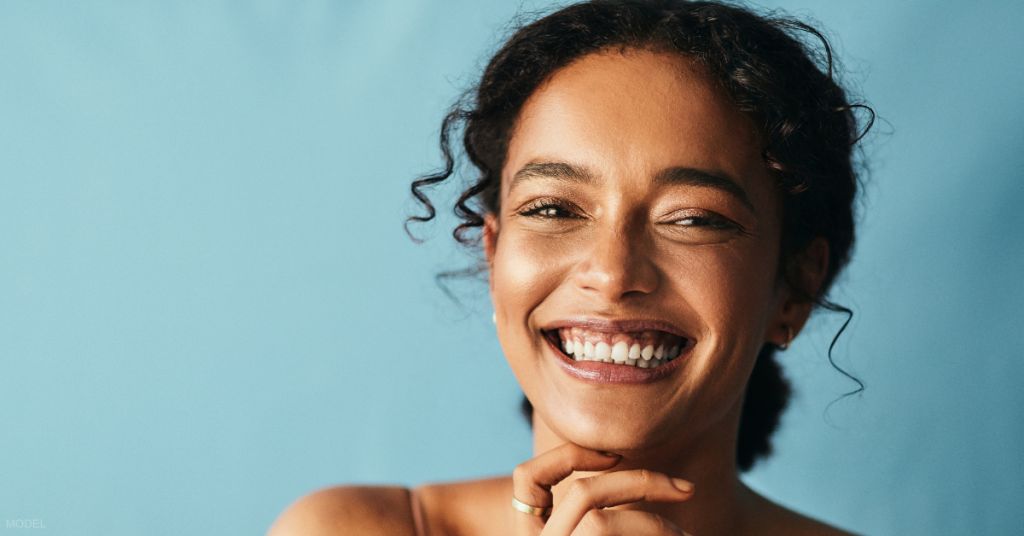 Young woman with smooth skin touching chin and smiling