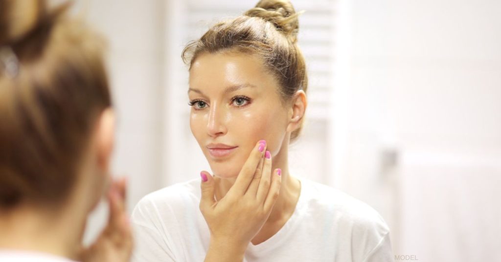 Woman with beautiful skin looking at her reflection in the mirror (model)