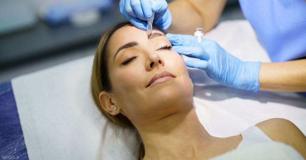 Woman laying on a treatment table getting her eyebrows microbladed (models)