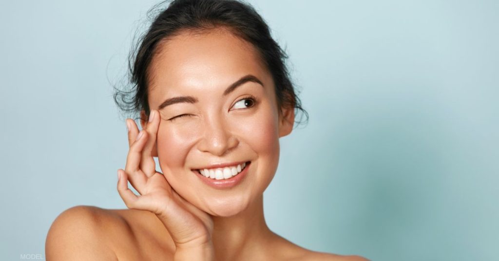 Woman smiling with one eye closed and touching her temple (model)