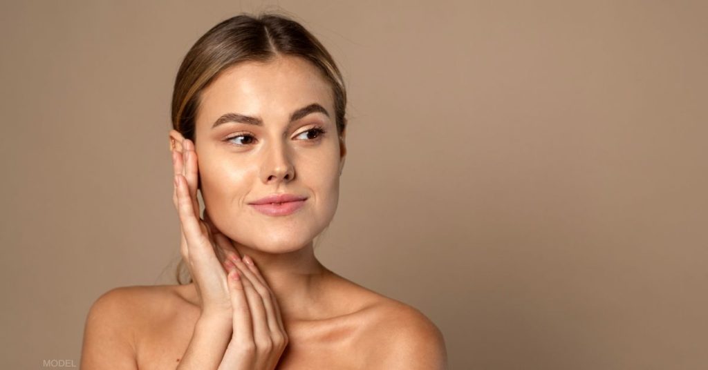 Woman with smooth skin looking off to the side and delicately touching her face (model)