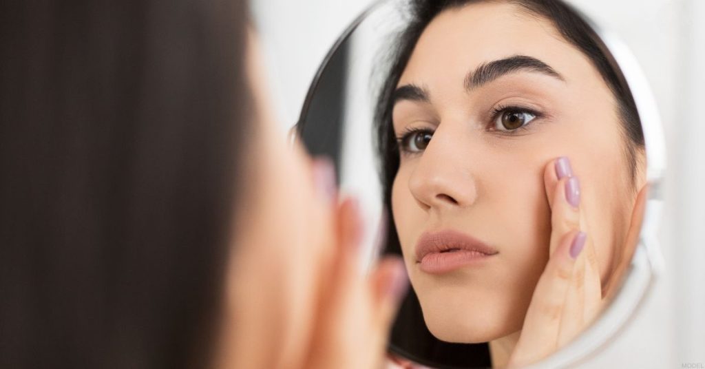 Woman looking at their face in the mirror (model)