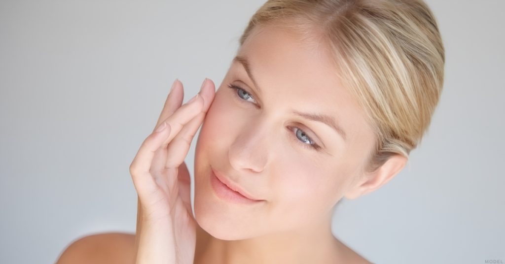 Woman gently touching her face after Botox and filler results. (model)